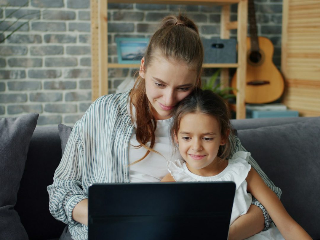 Una mamá y su hija mirando juntas la notebook en el sillón de casa